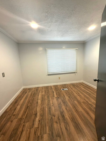 2491 Highway 89, Unit 114 Pleasant View, UT 84404 - Photo 9 of 18 Unfurnished room with dark wood finished floors, a textured ceiling, and crown molding