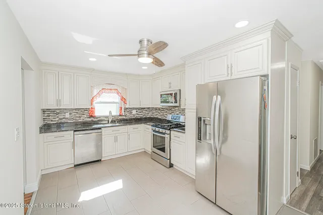 a kitchen with granite countertop stainless steel appliances a sink a refrigerator and white cabinets
