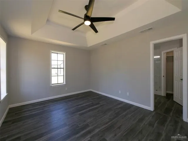 an empty room with wooden floor fan and windows