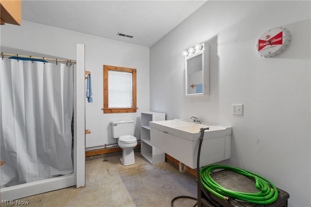 29395 Beitler Road Dennison, OH 44621 - Photo 26 of 33 Garage bathroom with a shower stall, vanity, unfinished concrete flooring, and a textured ceiling