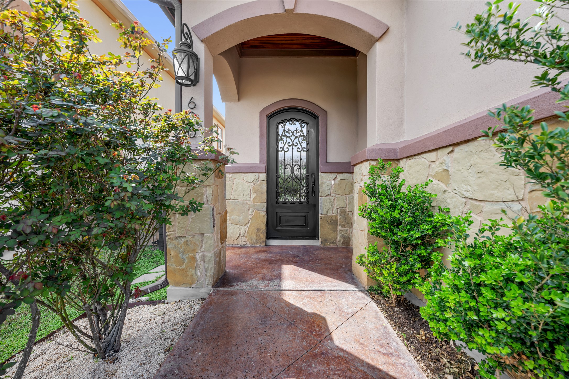 600 Samaripa Street Manor, TX 78653 - Photo 2 of 29 Charming covered entry with a beautifully designed wrought iron front door, complemented by stone detailing and a private walkway surrounded by lush landscaping, creating a warm and inviting first impression.