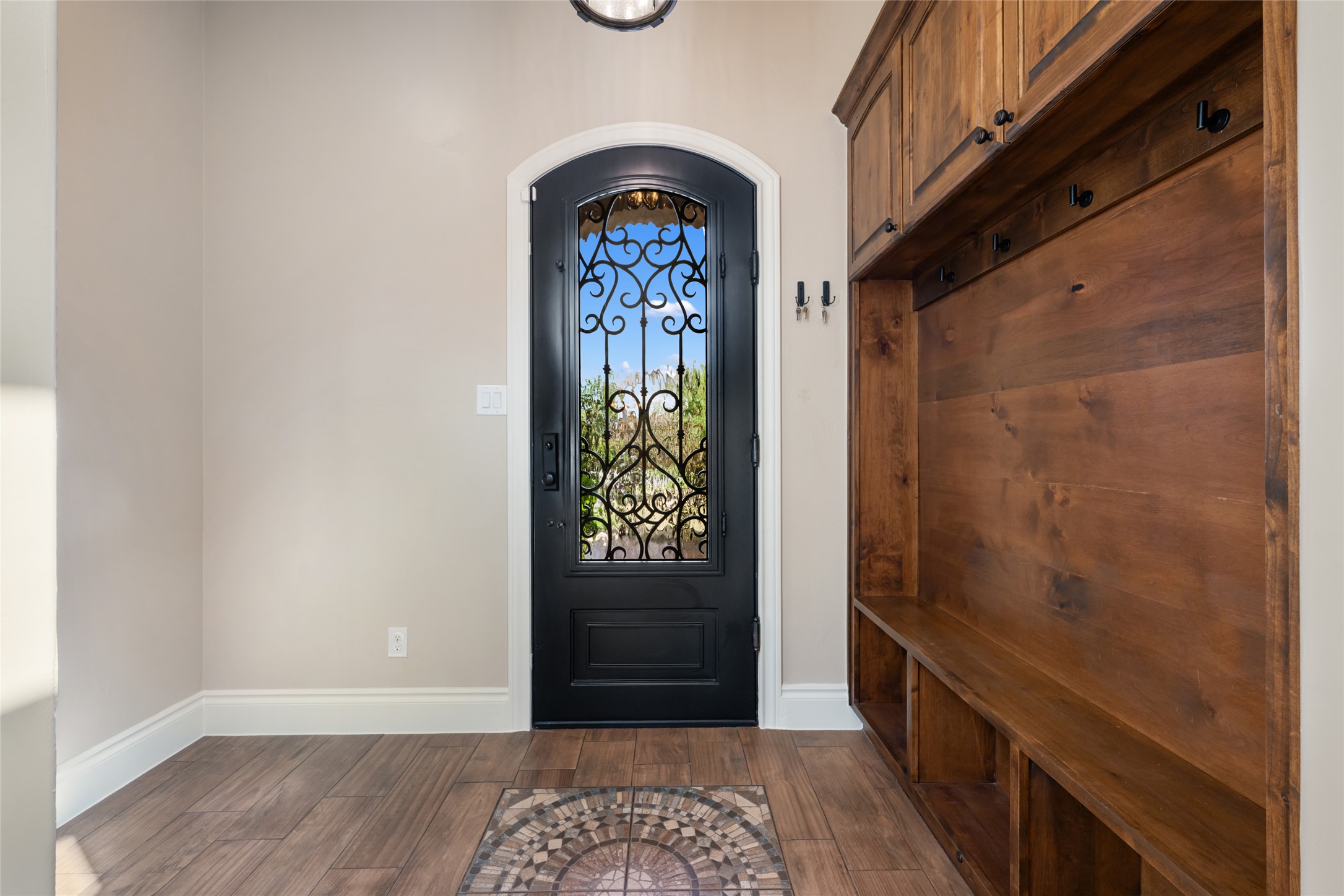 600 Samaripa Street Manor, TX 78653 - Photo 3 of 29 Inviting entryway showcasing an elegant wrought iron front door, durable wood-look tile flooring, and a custom built-in mud bench with storage and hooks—perfect for everyday organization.