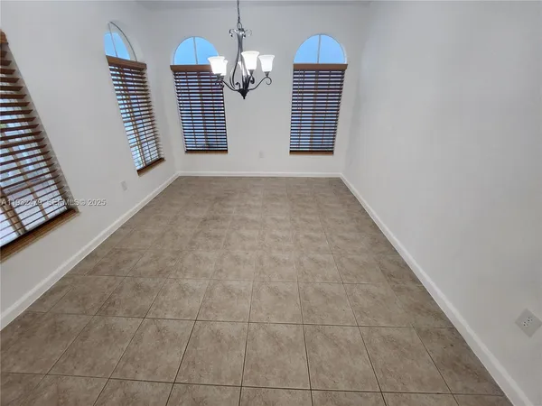 an empty room with kitchen view and a chandelier