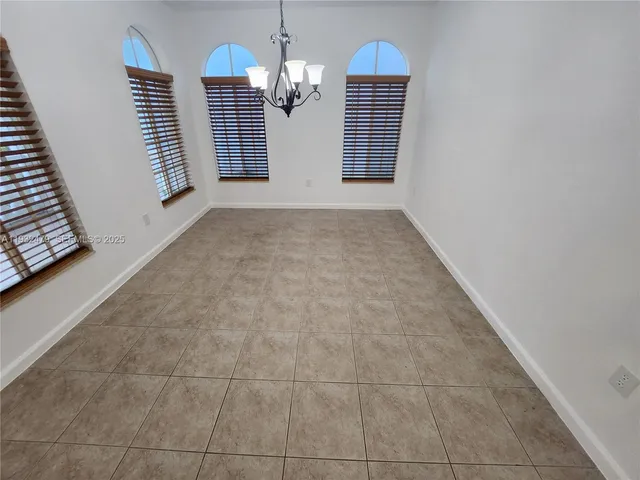 an empty room with kitchen view and a chandelier