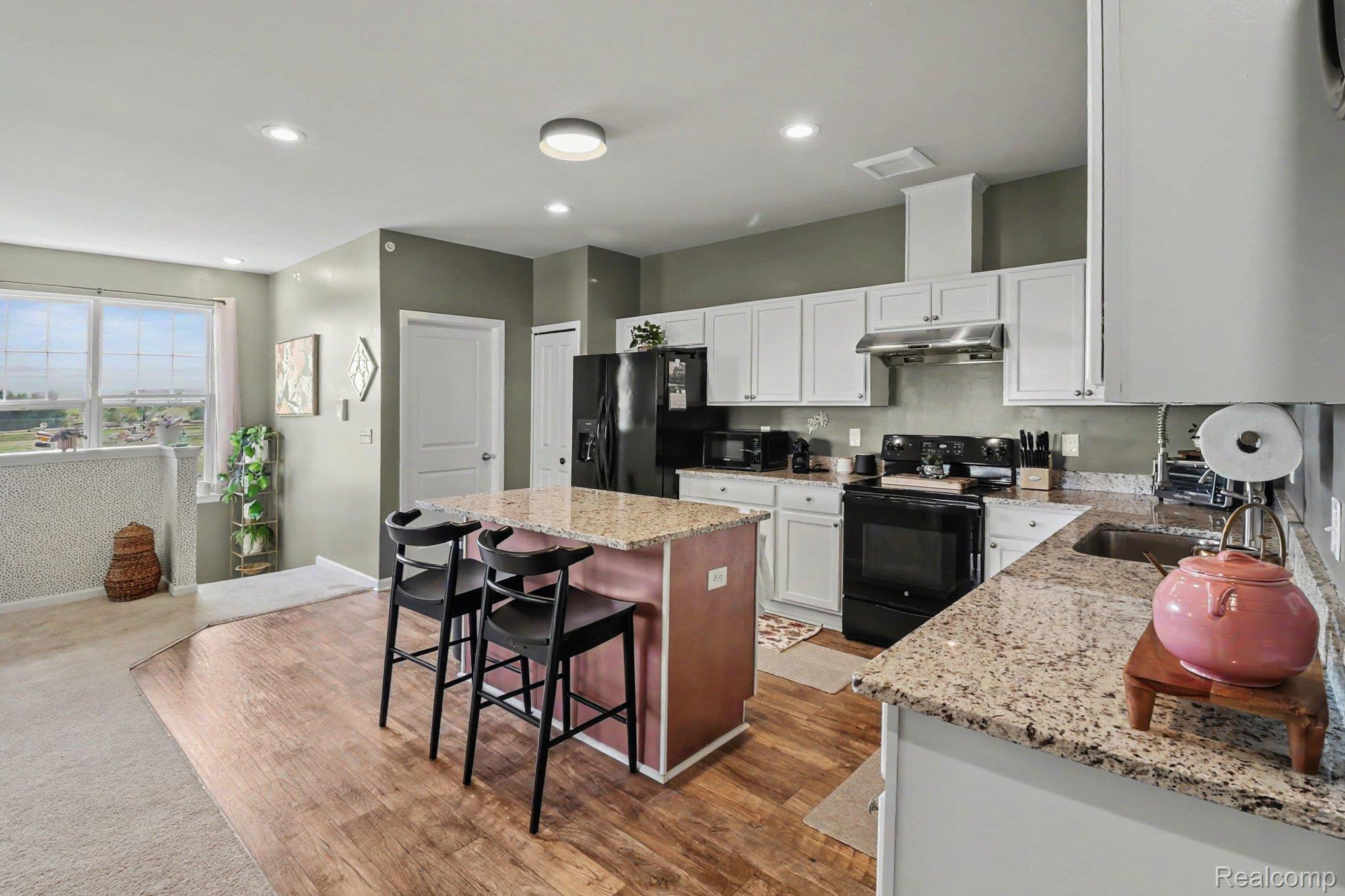 9864 Ridge Run Street Howell, MI 48855 - Photo 14 of 23 Dual tone kitchen with black appliances, a center island, light stone counters, a kitchen bar, and recessed lighting