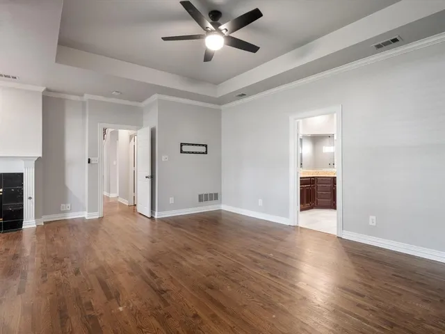 a view of an empty room with wooden floor and a ceiling fan