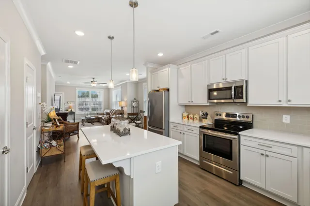 a kitchen with stainless steel appliances kitchen island granite countertop a stove a sink a microwave a refrigerator and white cabinets with wooden floor