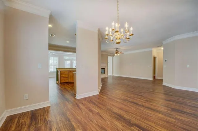 a view of an empty room and kitchen with wooden floor
