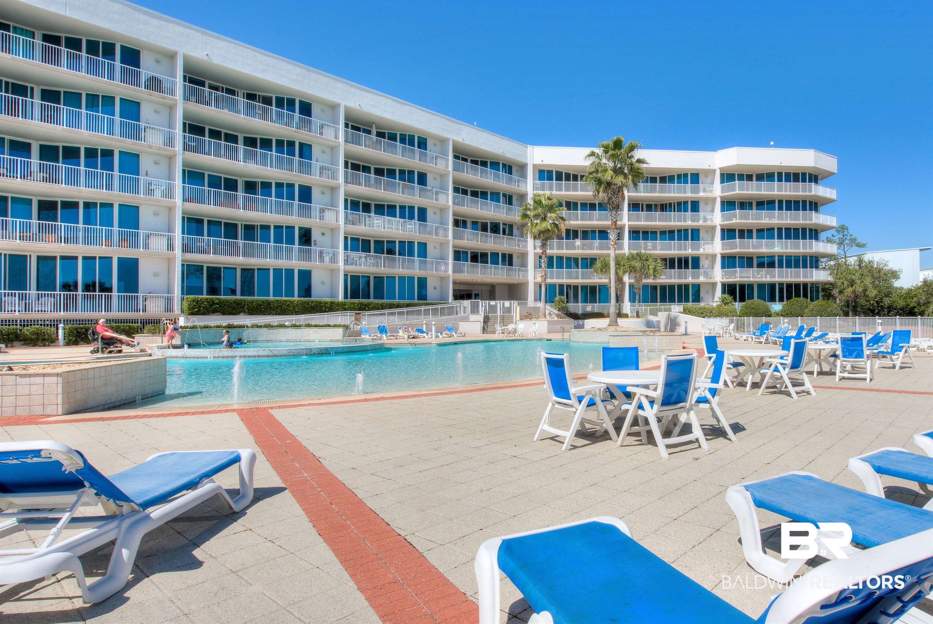 27800 Canal Road, Unit 411 Orange Beach, AL 36561 - Photo 49 of 49 Expansive resort-style pool deck with a large swimming pool, surrounded by a paver patio with seating areas, and featuring a multi-story condominium building with private balconies