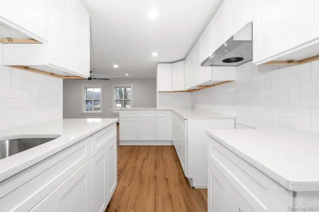 a kitchen with a sink dishwasher a stove and white cabinets with wooden floor