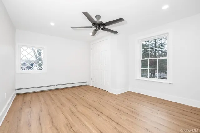 an empty room with wooden floor a ceiling fan and windows
