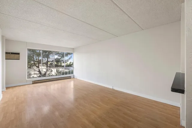 a view of empty room with wooden floor and kitchen
