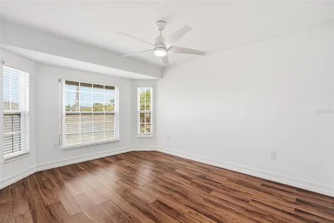 an empty room with wooden floor fan and windows