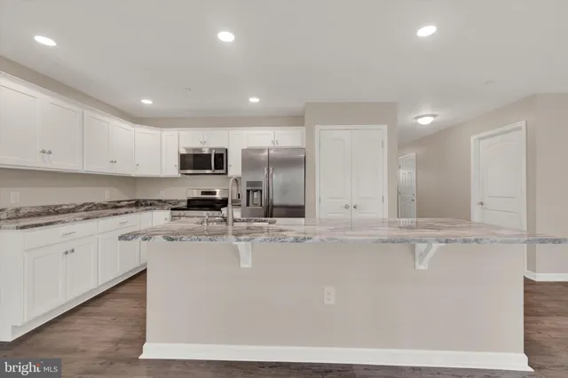 a large kitchen with granite countertop a stove a sink a refrigerator and white cabinets with wooden floor