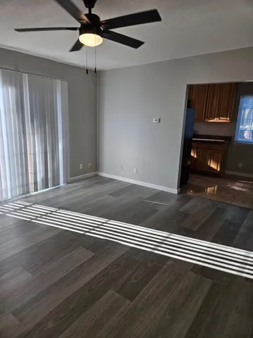 an empty room with wooden floor chandelier fan and windows