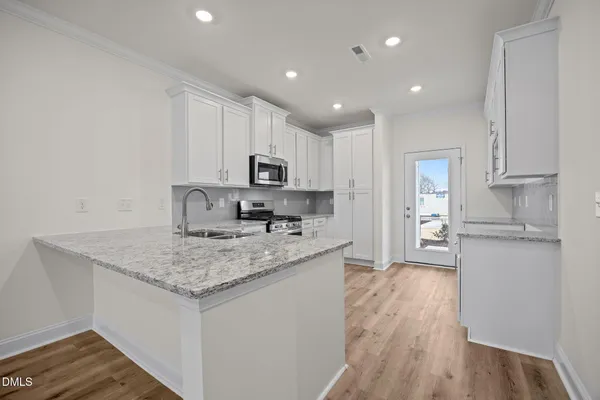 a kitchen with a sink dishwasher a refrigerator and white cabinets with wooden floor