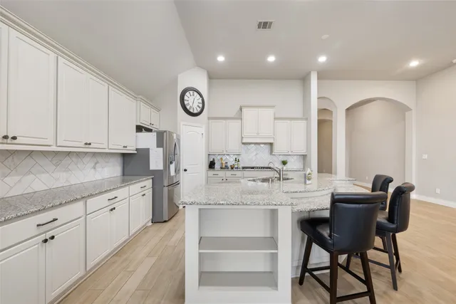 a large kitchen with stainless steel appliances kitchen island granite countertop a table chairs in it and white cabinets
