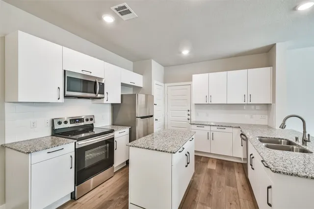 a kitchen with stainless steel appliances granite countertop a stove top oven a sink a refrigerator and white cabinets with wooden floor