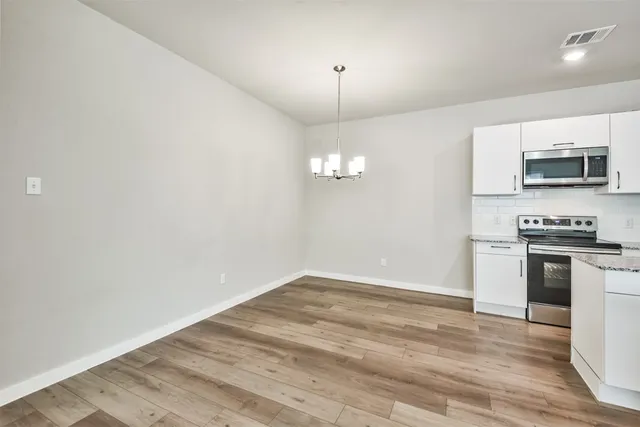 an empty room with wooden floor kitchen view and a window