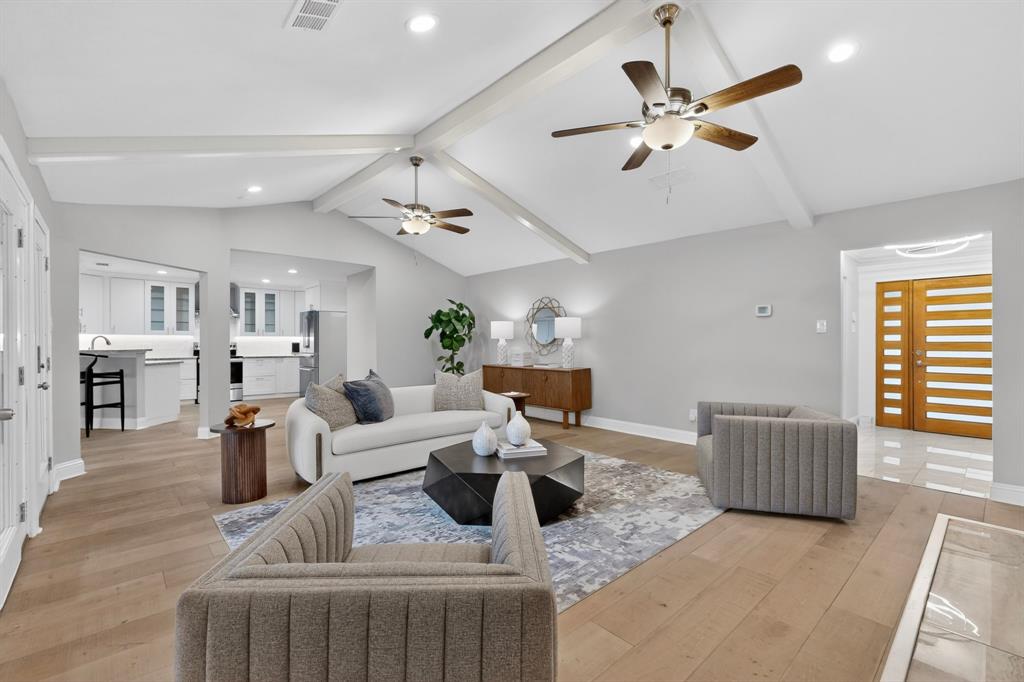 7631 Meadow Road Dallas, TX 75230 - Photo 8 of 40 A cozy family room with a high ceiling and two ceiling fans, seamlessly leading into a contemporary kitchen area.