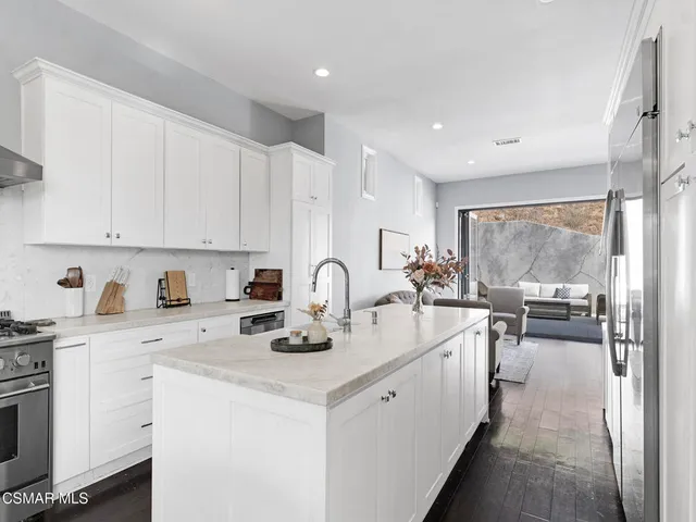 a view of a kitchen with kitchen island a sink a stove and white cabinets with wooden floor