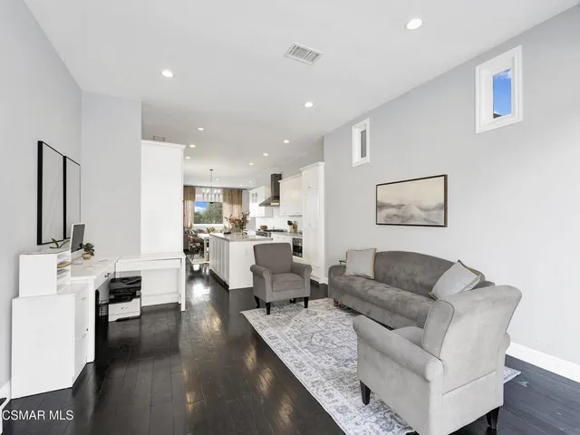 a living room with couches and kitchen view with wooden floor