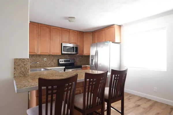 a kitchen with stainless steel appliances granite countertop a stove a refrigerator a sink a dining table and chairs
