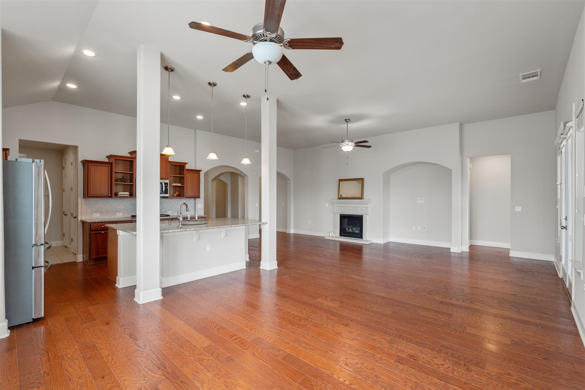 3516 Venezia View Leander, TX 78641 - Photo 5 of 40 Living room featuring ceiling fan, a fireplace with raised hearth, light wood-style flooring, vaulted ceiling, and arched walkways