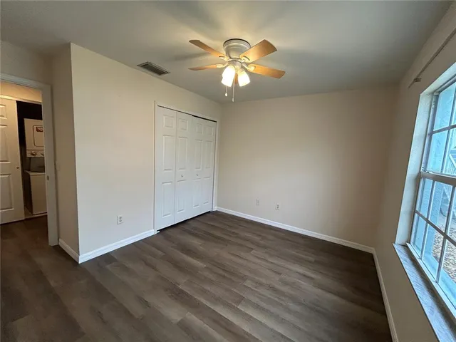 an empty room with wooden floor chandelier fan and windows