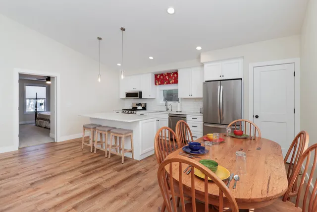 a very nice looking dining room with kitchen island stainless steel appliances a refrigerator a stove a sink a dining table and chairs with wooden floor