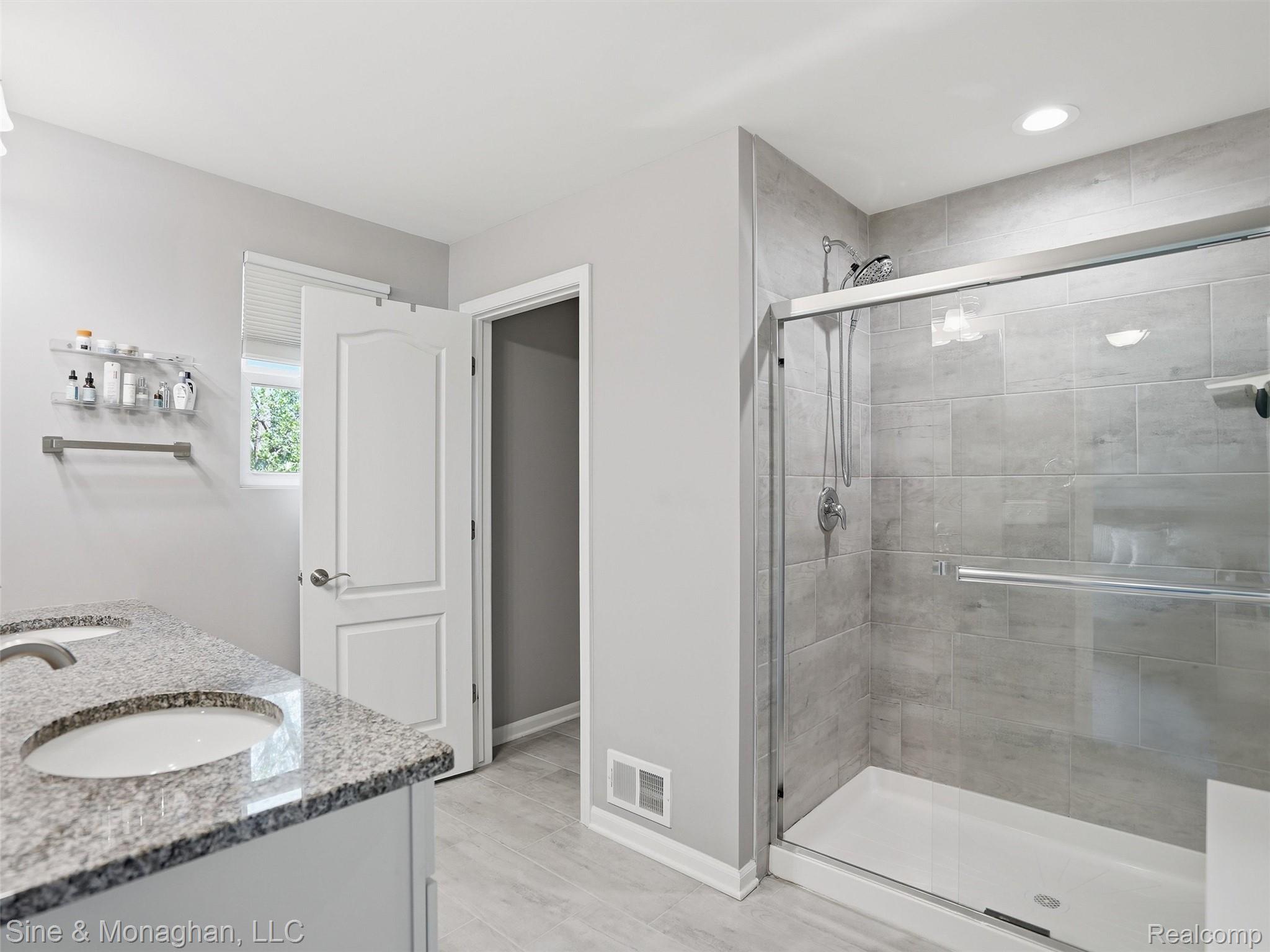 24827 Ivy Road Novi, MI 48375 - Photo 19 of 38 Bathroom featuring a dual-sink vanity with a speckled countertop, a glass-enclosed shower with tile surround, and light wood-finish flooring