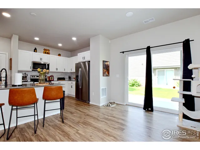 a kitchen with stainless steel appliances kitchen island granite countertop a refrigerator a stove top oven a sink a dining table and chairs with wooden floor