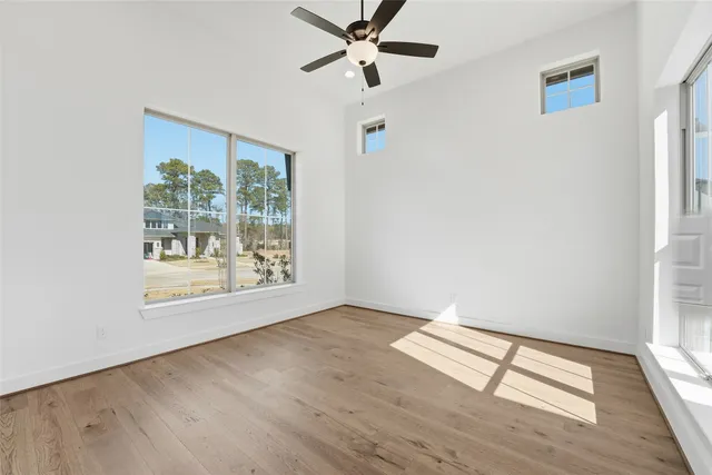 an empty room with wooden floor fan and windows