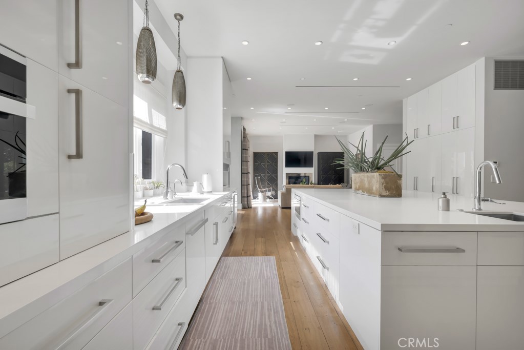 17950 Rancho Street Encino, CA 91316 - Photo 22 of 75 a large white kitchen with a large counter top a sink a window and stainless steel appliances