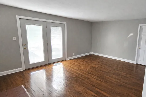 a view of an empty room with wooden floor and a window