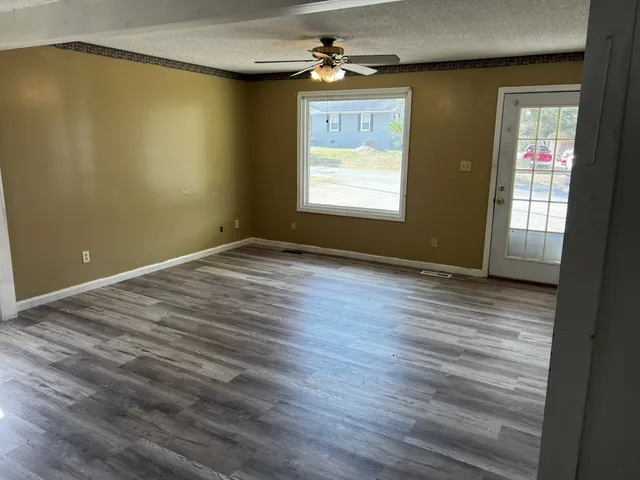 an empty room with wooden floor chandelier fan and windows