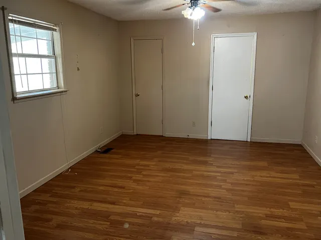 an empty room with wooden floor chandelier fan and windows