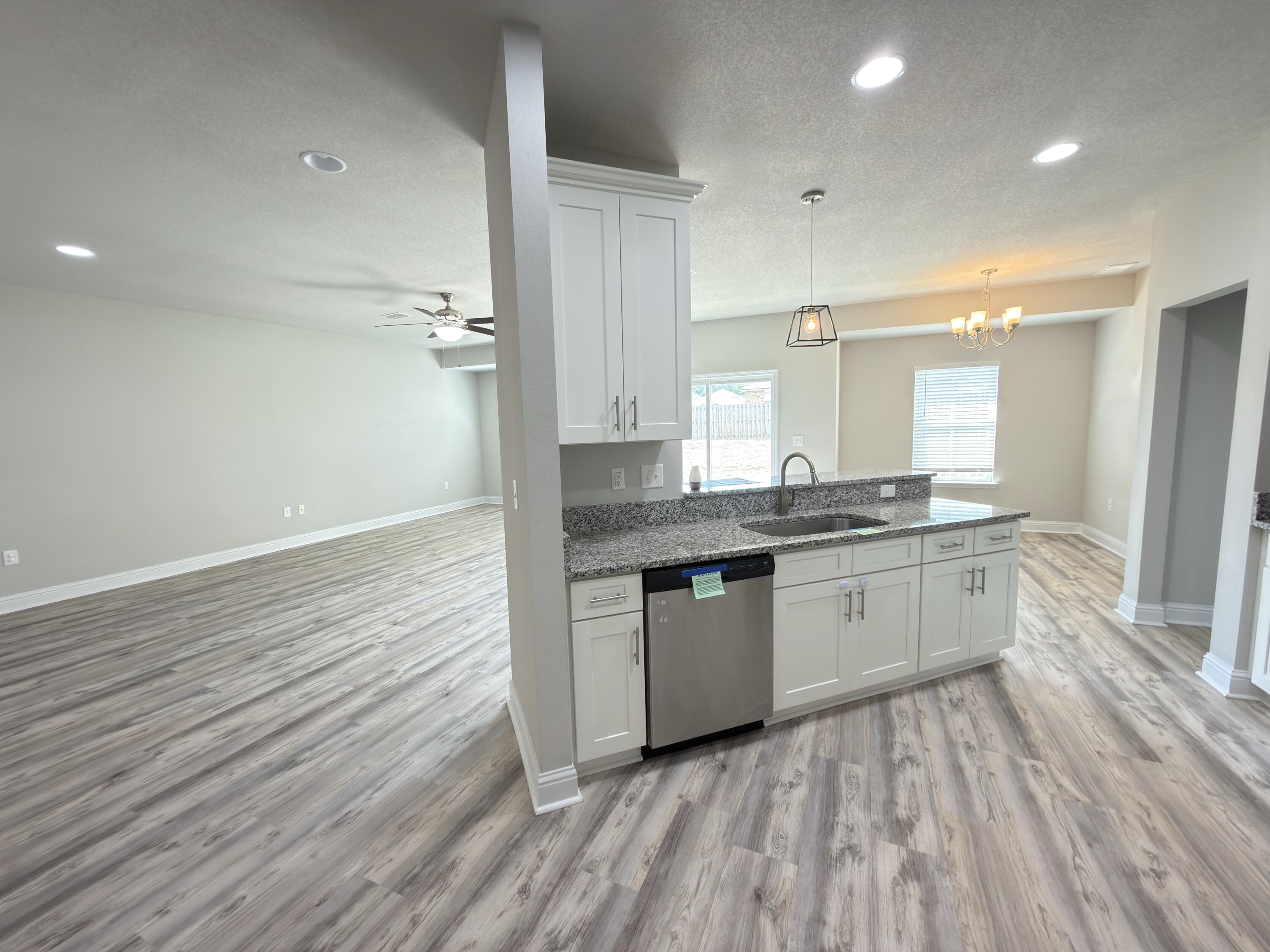 5281 Moore Loop Crestview, FL 32536 - Photo 5 of 28 a large kitchen with granite countertop a stove top oven a sink and white cabinets with wooden floor