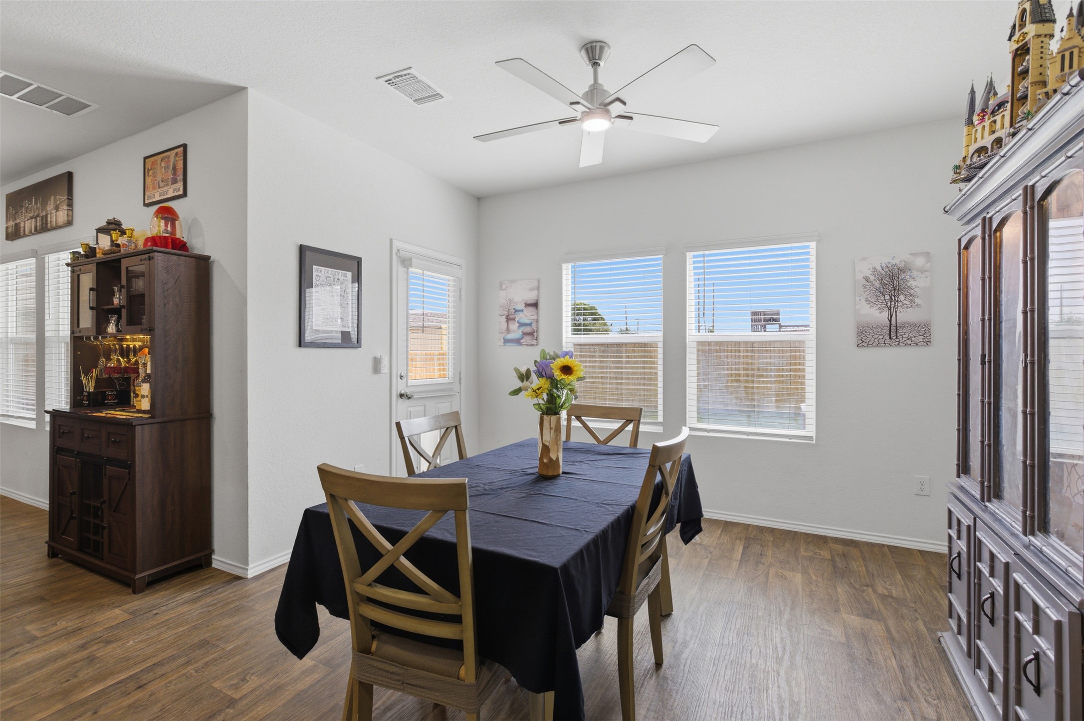 19017 Romano Drive Elgin, TX 78621 - Photo 12 of 33 Dining area featuring wood-finish flooring, a ceiling fan, multiple windows with horizontal blinds, and a white paneled door