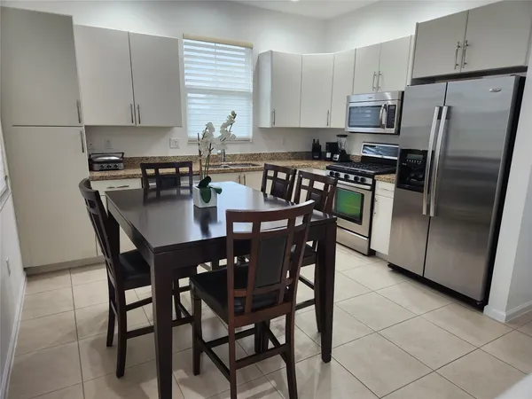 a kitchen with stainless steel appliances granite countertop a dining table chairs refrigerator and sink