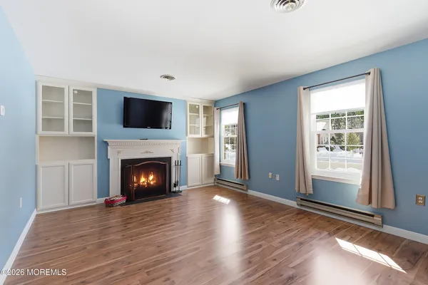a view of an empty room with wooden floor fireplace and a window