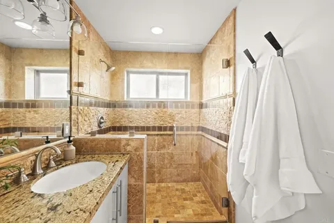 a bathroom with a granite countertop sink a mirror a bathtub and shower