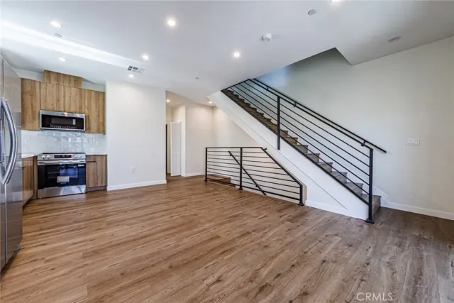 an empty room with wooden floor and a kitchen view