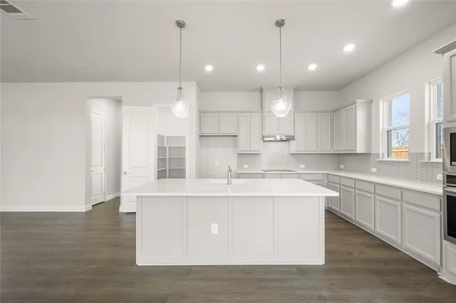 a large kitchen with kitchen island a stove a sink a center island and wooden floor