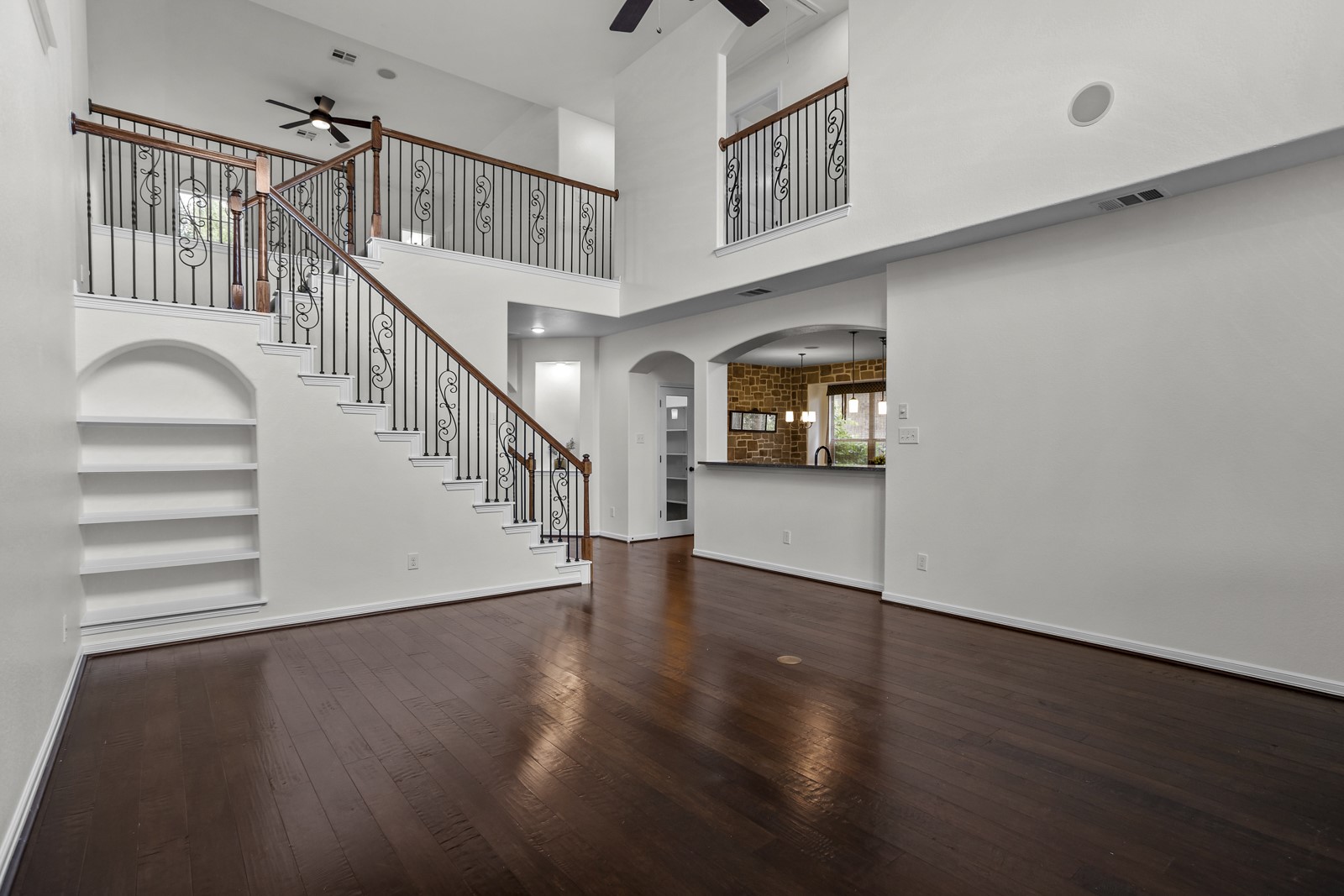 245 Razzmatazz Trail Buda, TX 78610 - Photo 15 of 37 Two-story interior featuring a grand staircase with decorative wrought iron spindles and wood handrails, dark wood-finish flooring, a built-in arched bookshelf, and a loft overlook