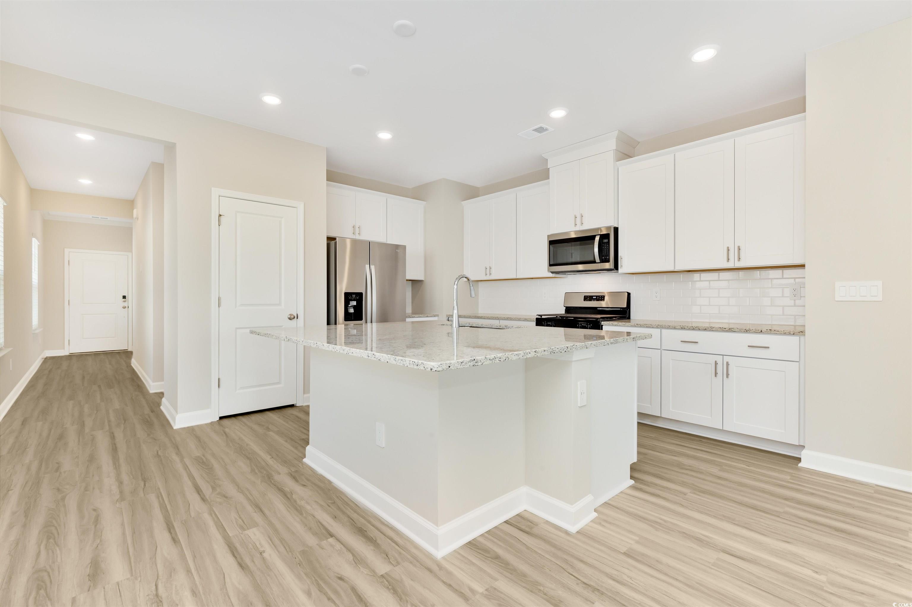 826 Cypress Preserve Circle Longs, SC 29568 - Photo 4 of 27 Kitchen featuring white cabinetry, a center island with sink, light wood-type flooring, stainless steel appliances, and decorative backsplash