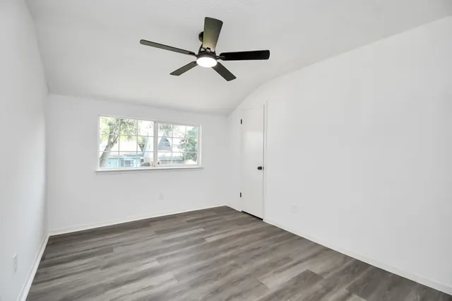 an empty room with wooden floor fan and windows
