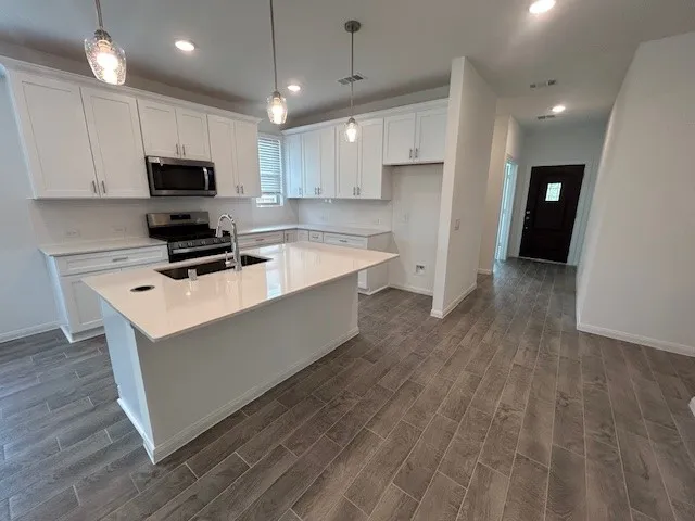 a kitchen with stainless steel appliances a stove a refrigerator a sink a microwave oven and white cabinets with wooden floor