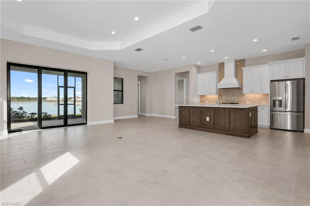 3993 Perseus Street Naples, FL 34120 - Photo 19 of 20 Kitchen with open floor plan, stainless steel fridge, white cabinetry, a water view, and an island with sink