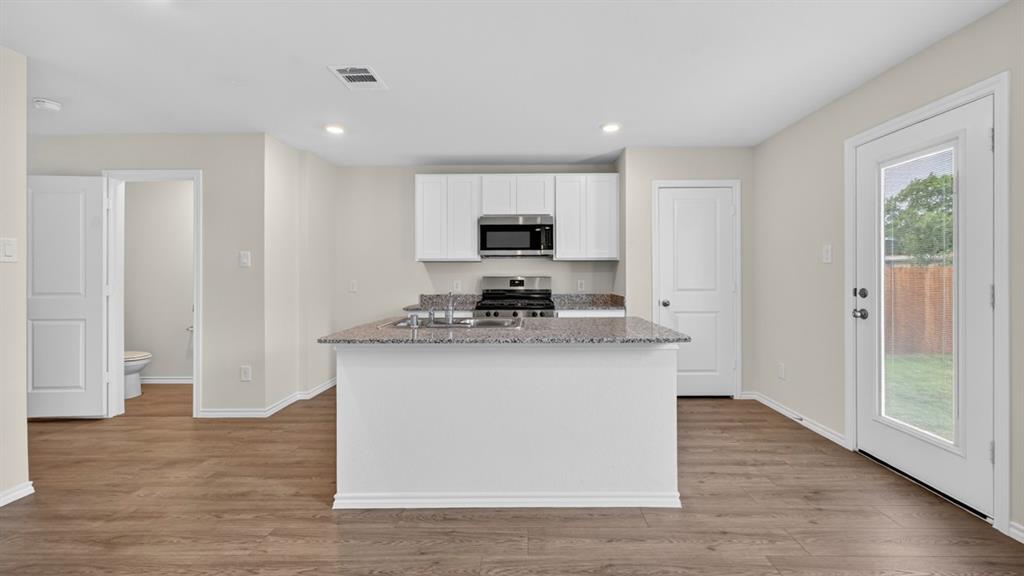 3534 Spring Time Street Forney, TX 75126 - Photo 4 of 24 Kitchen with a central island featuring a granite countertop, white cabinetry, stainless steel appliances, and wood-finish flooring